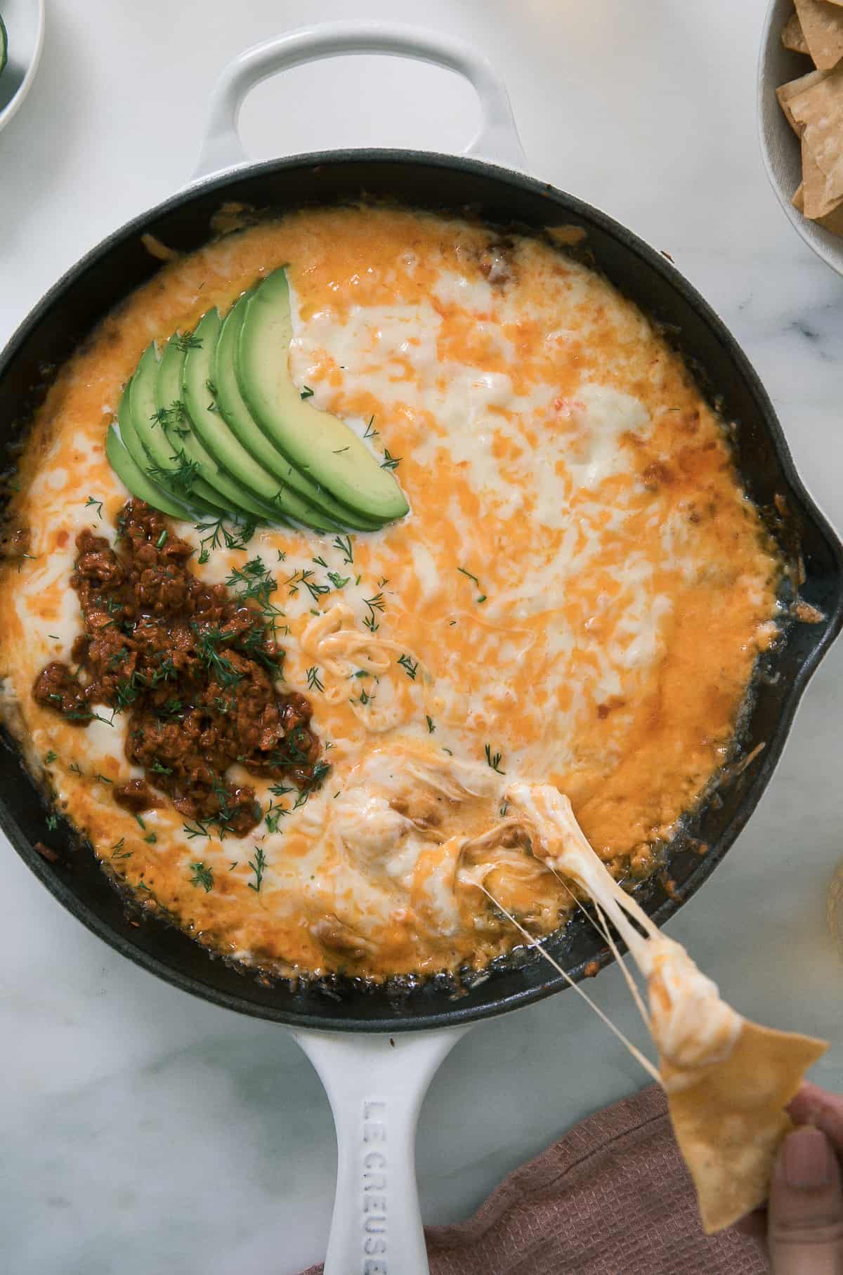 Skillet of queso fundido topped with chorizo and avocado.