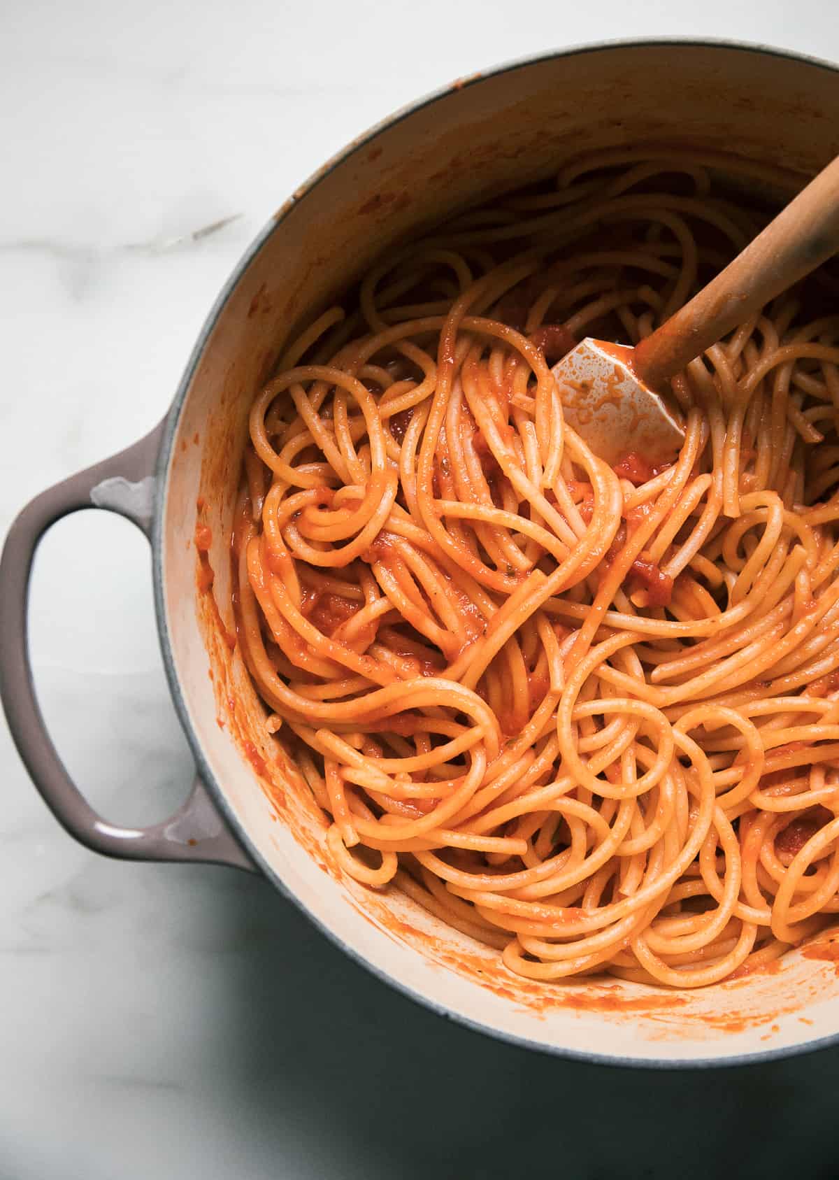 Pot with noodles and marinara being tossed together. 