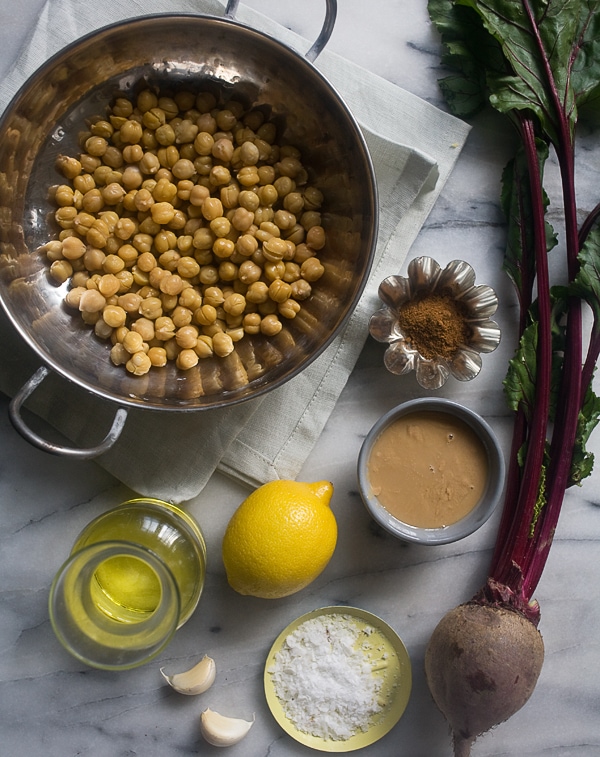 Garbanzo beans, cumin, tahini, beets, lemon, olive oil and salt on a counter top. 