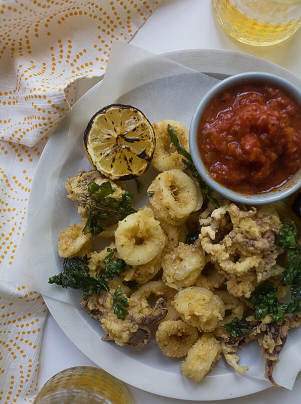 Fried Calamari on a plate with a grilled lemon and marinara sauce. 