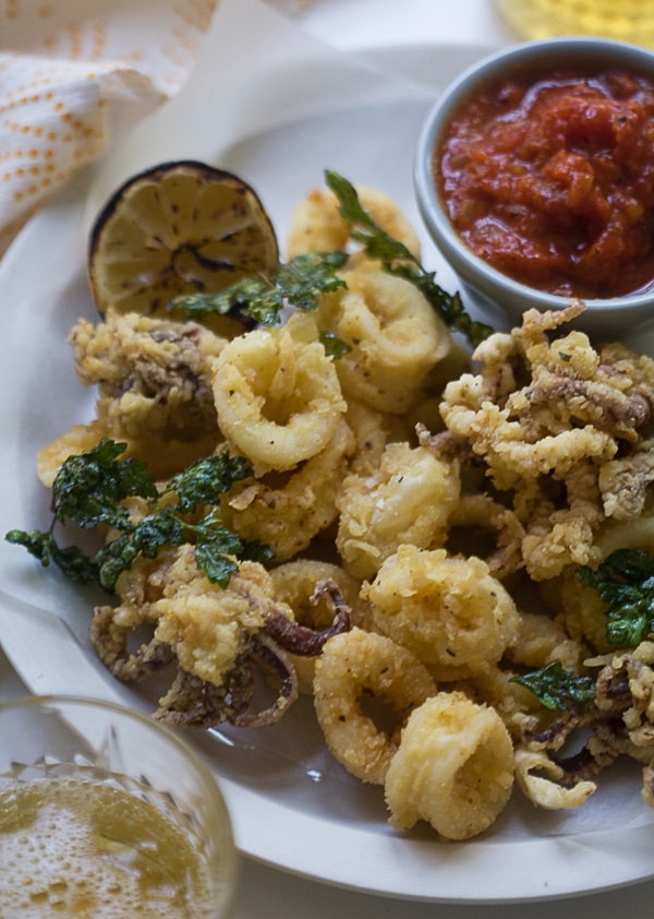 Fried Calamari on a plate with a grilled lemon and marinara sauce. 