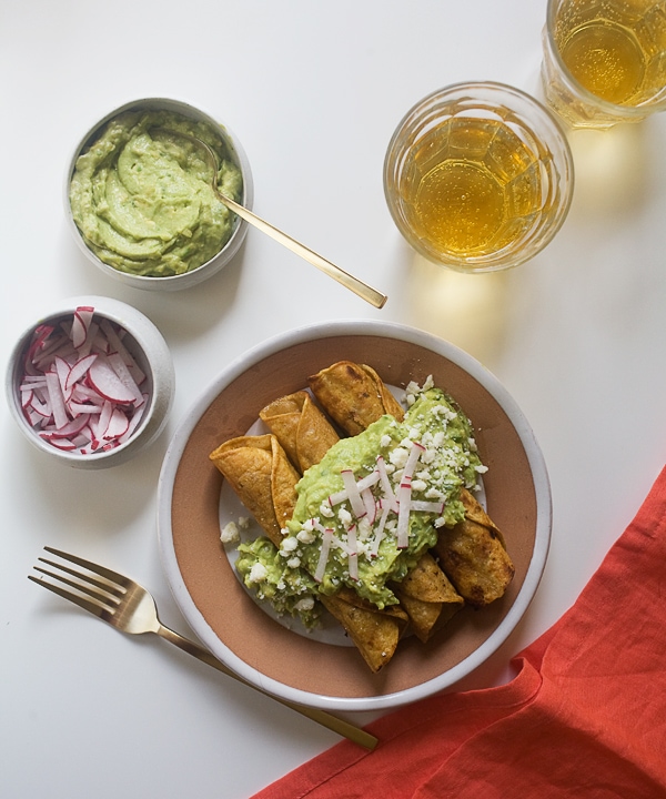 Chicken Taquitos with Avocado Crema on a plate topped with radishes. 