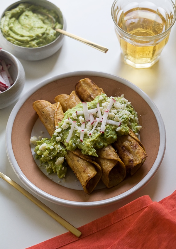 Chicken Taquitos with Avocado Crema on a plate topped with radishes. 