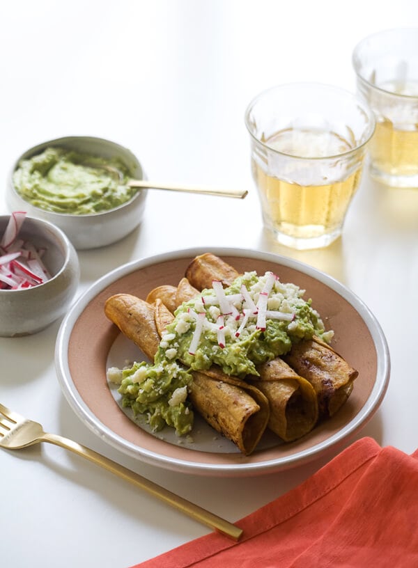 Chicken Taquitos with Avocado Crema on a plate topped with radishes. 