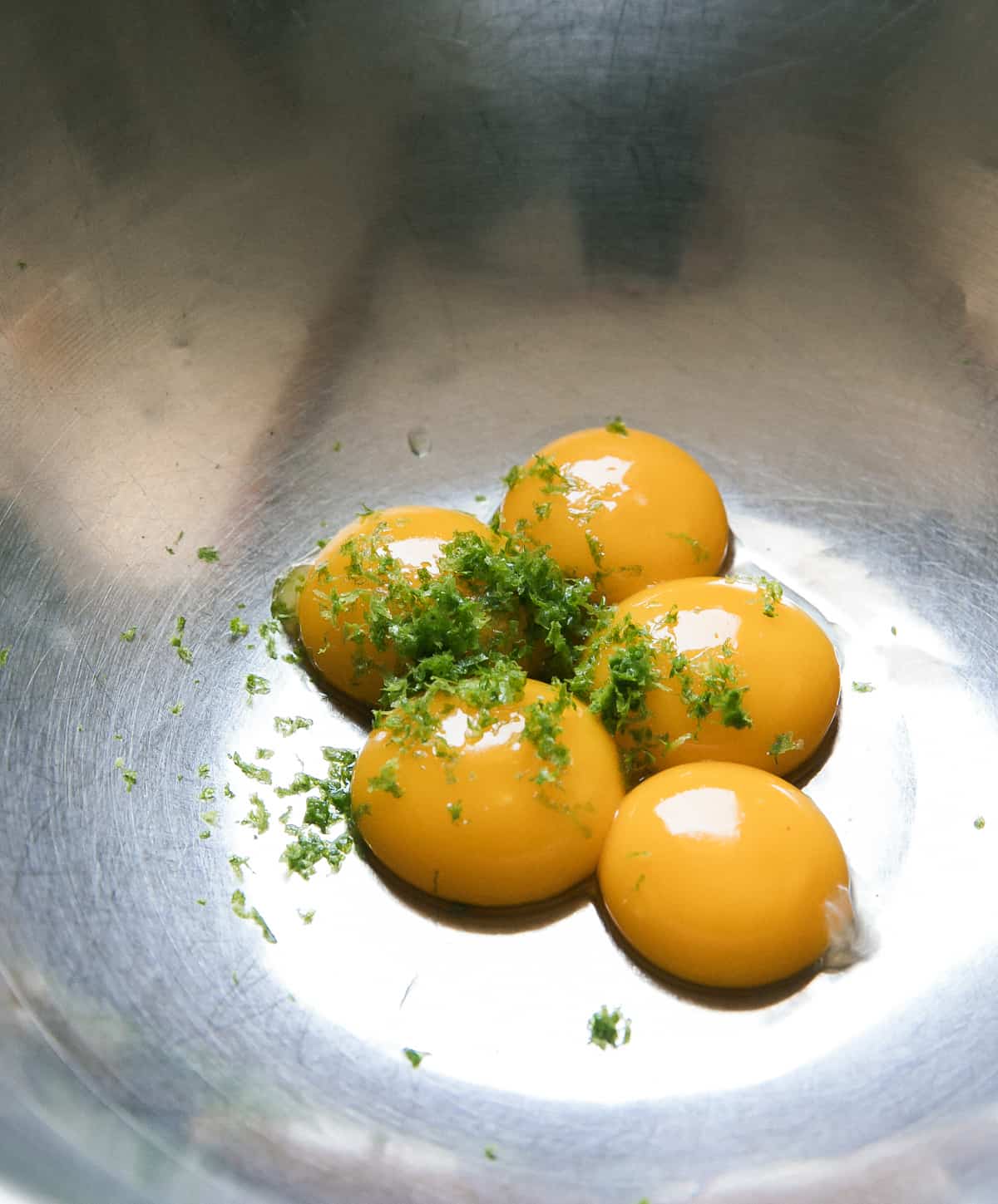 Egg yolks in bowl with lime zest. 