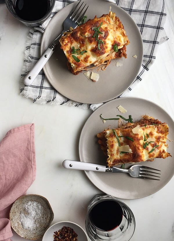 Lasagna for two. Slices on plates with basil on top. 