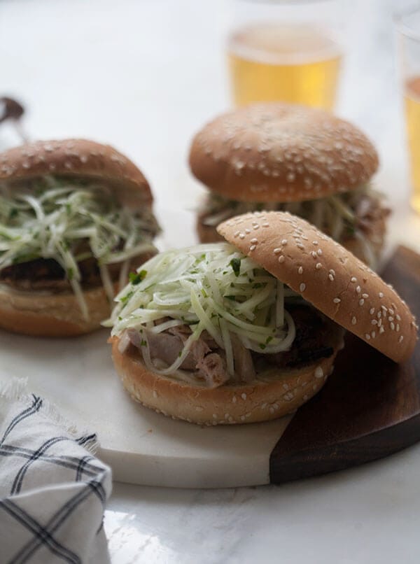 Jerk Chicken Sandwich with Jicama Slaw on serving board with beer. 