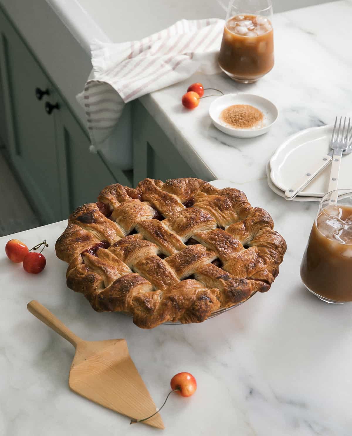 A whole classic cherry pie on the counter with an iced coffee nearby.