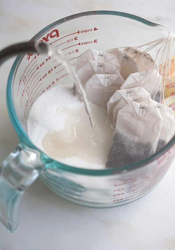 Hot water going into measuring cup with tea bags and sugar.