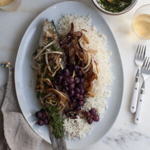 Overhead image of whole branzino with fennel, grapes, and charred salsa verde on a serving platter with rice.