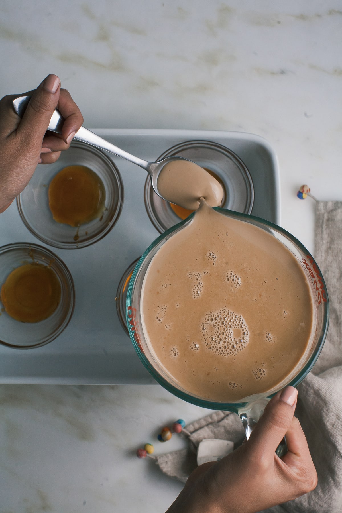 Flan filling in a measuring cup spooned into ramekins.