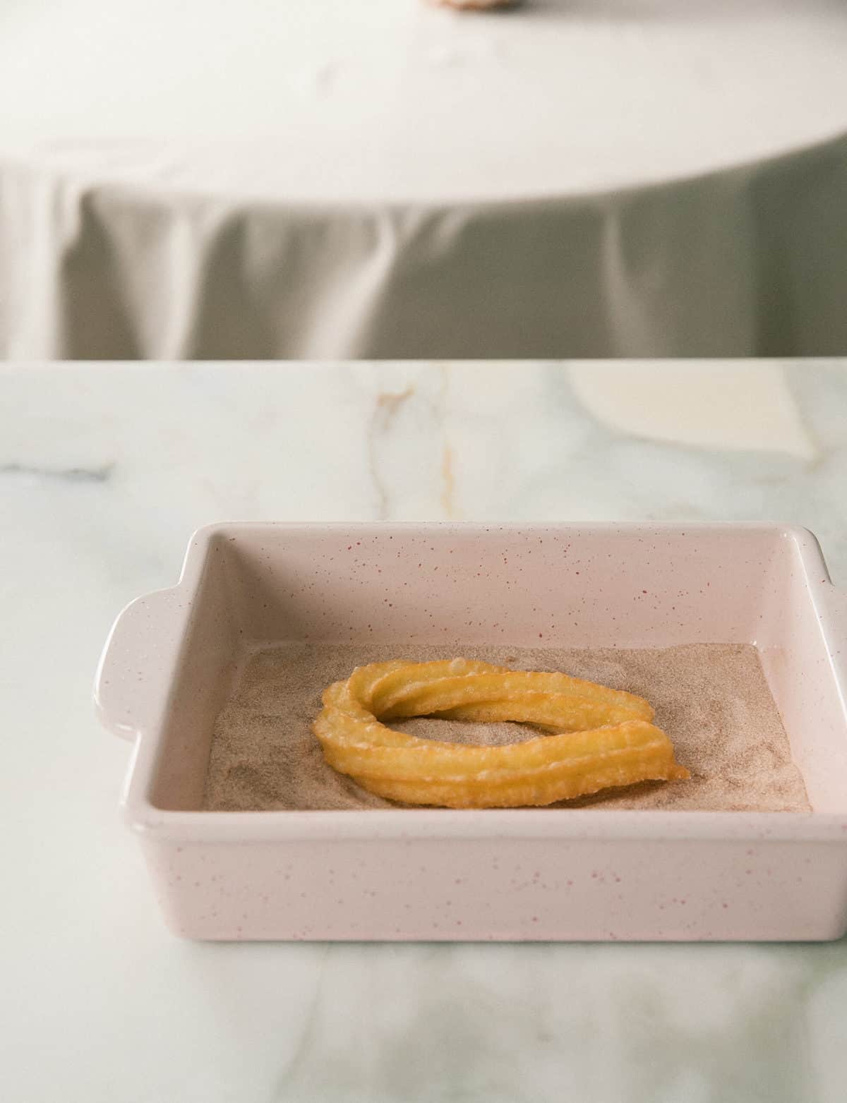 Churros being rolled in cinnamon sugar.