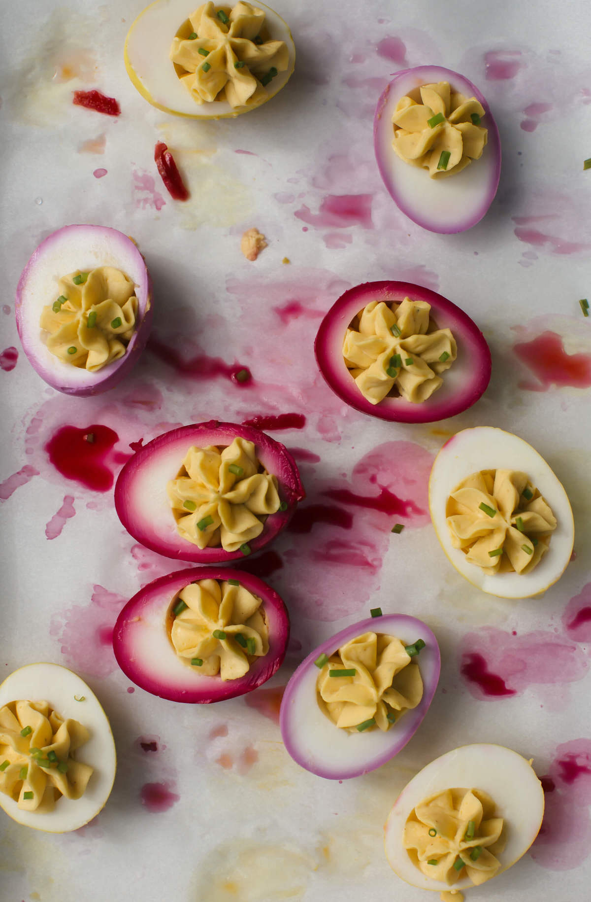 Naturally dyed pickled deviled eggs on parchment paper. 