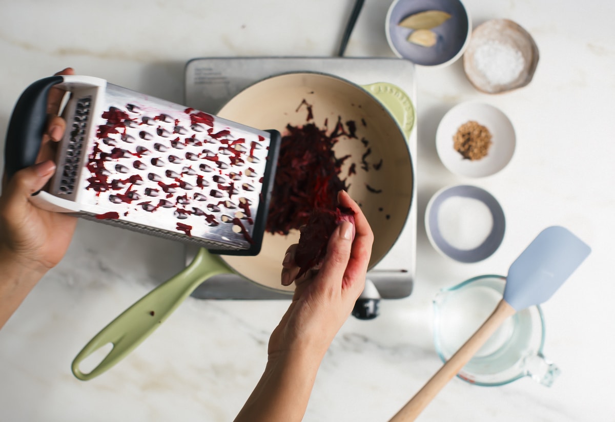 Hand holding grated beets and a grater. 