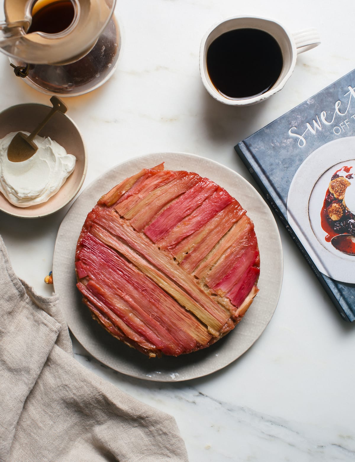 Rhubarb upside down cake on a platter with a cookbook near by.