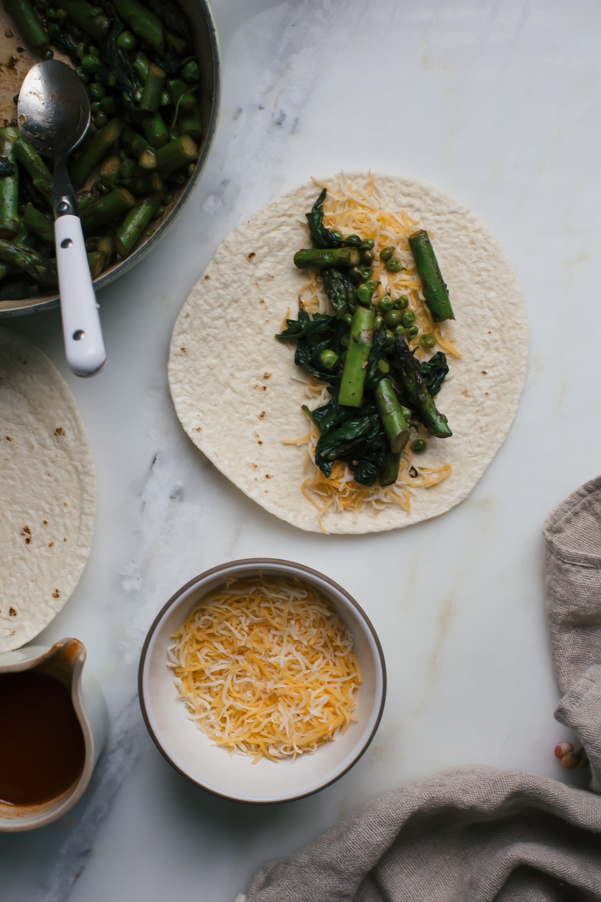 Tortilla on a counter topped with shredded cheese and cooked vegetable filling. 