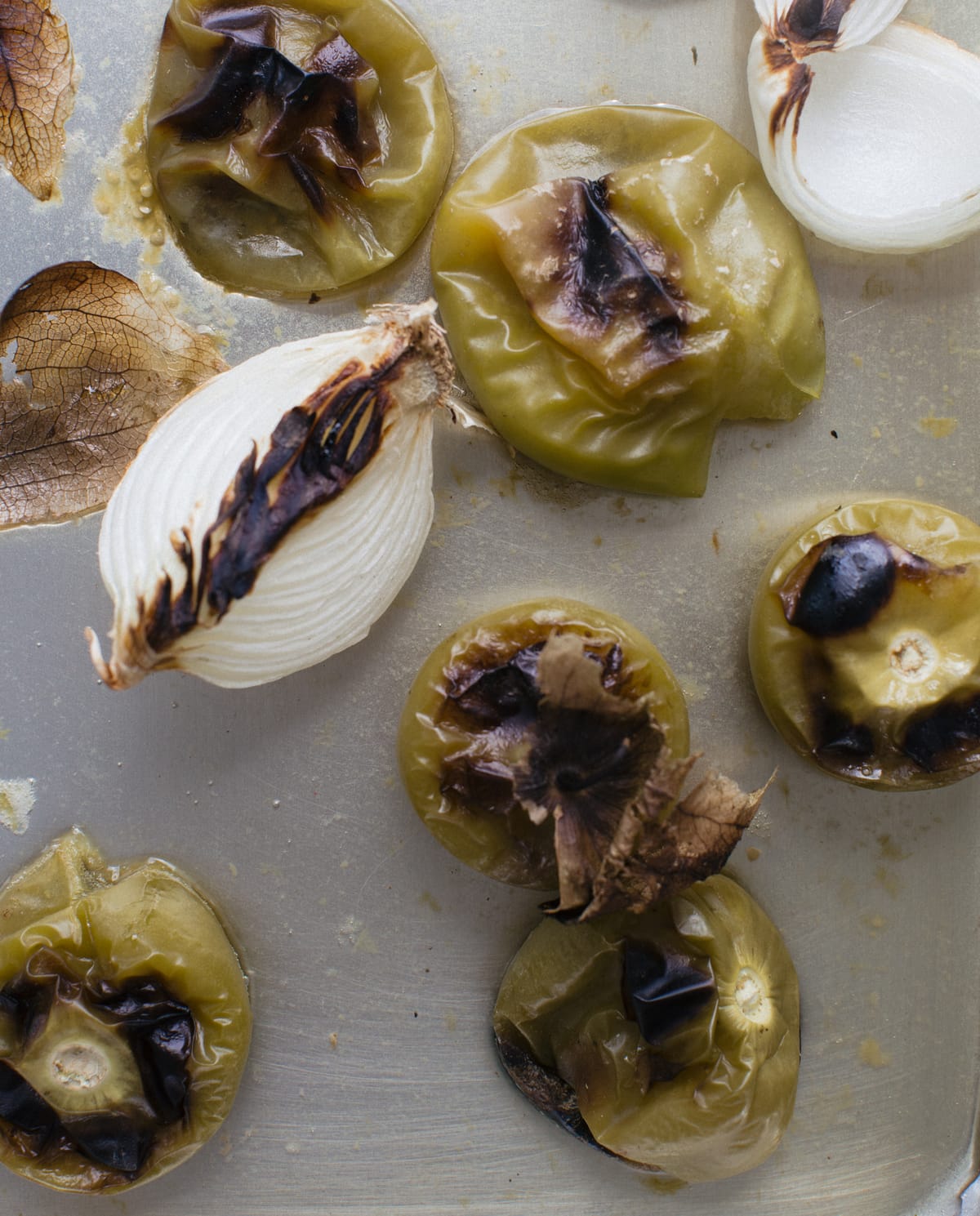 Charred onions and tomatillos on a sheet pan.