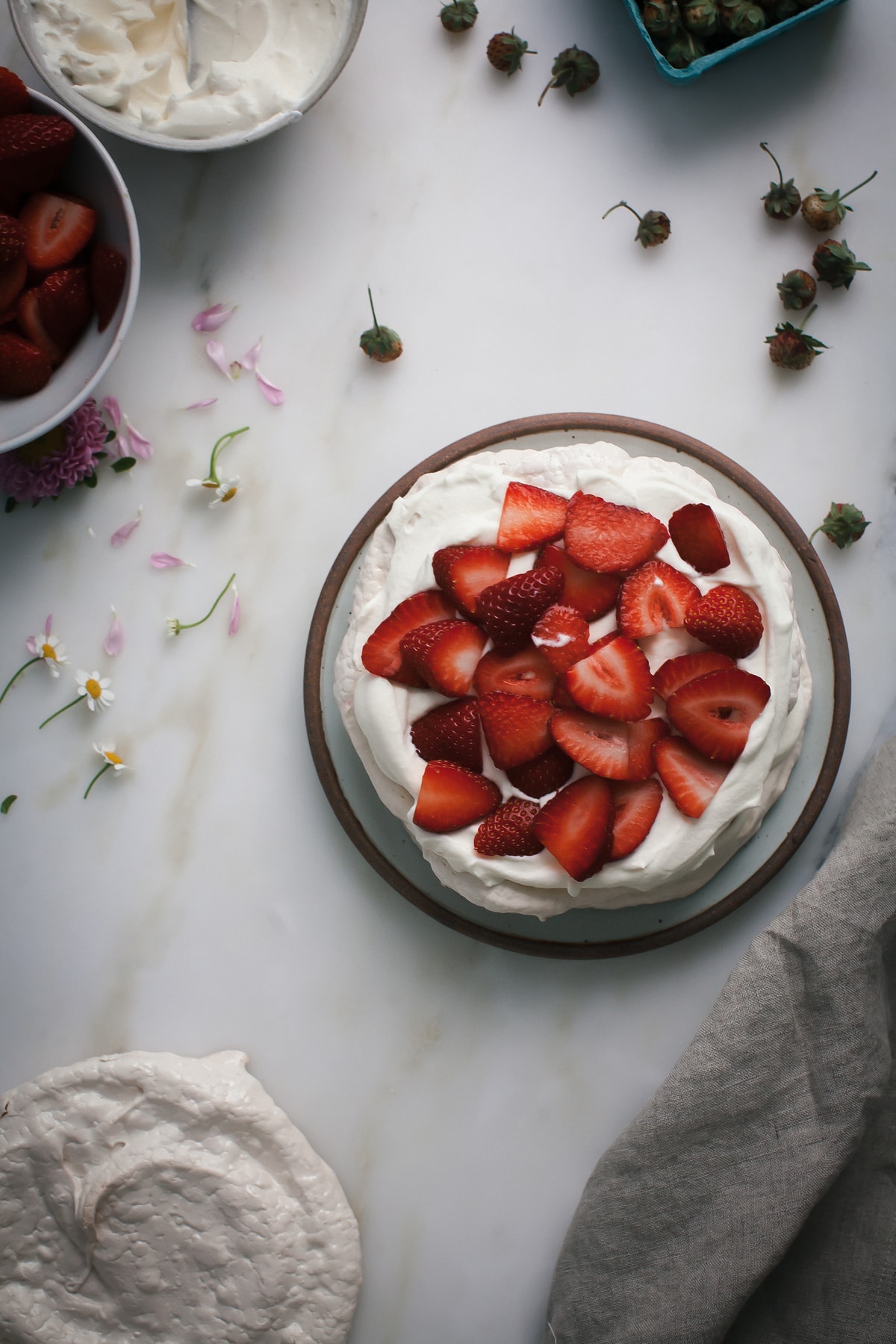 Pavlova topped with whipped cream and sliced strawberries. 