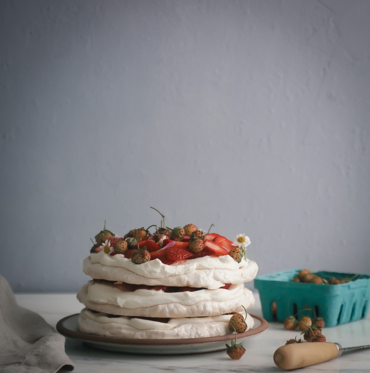 Side view of a Eton Mess on a plate with fresh fruit on a counter.