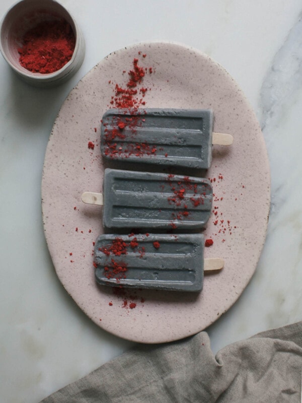 Black sesame popsicles on a plate with freeze-dried strawberries.