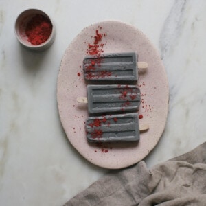 Black Sesame Popsicles on a platter topped with freeze dried strawberries.