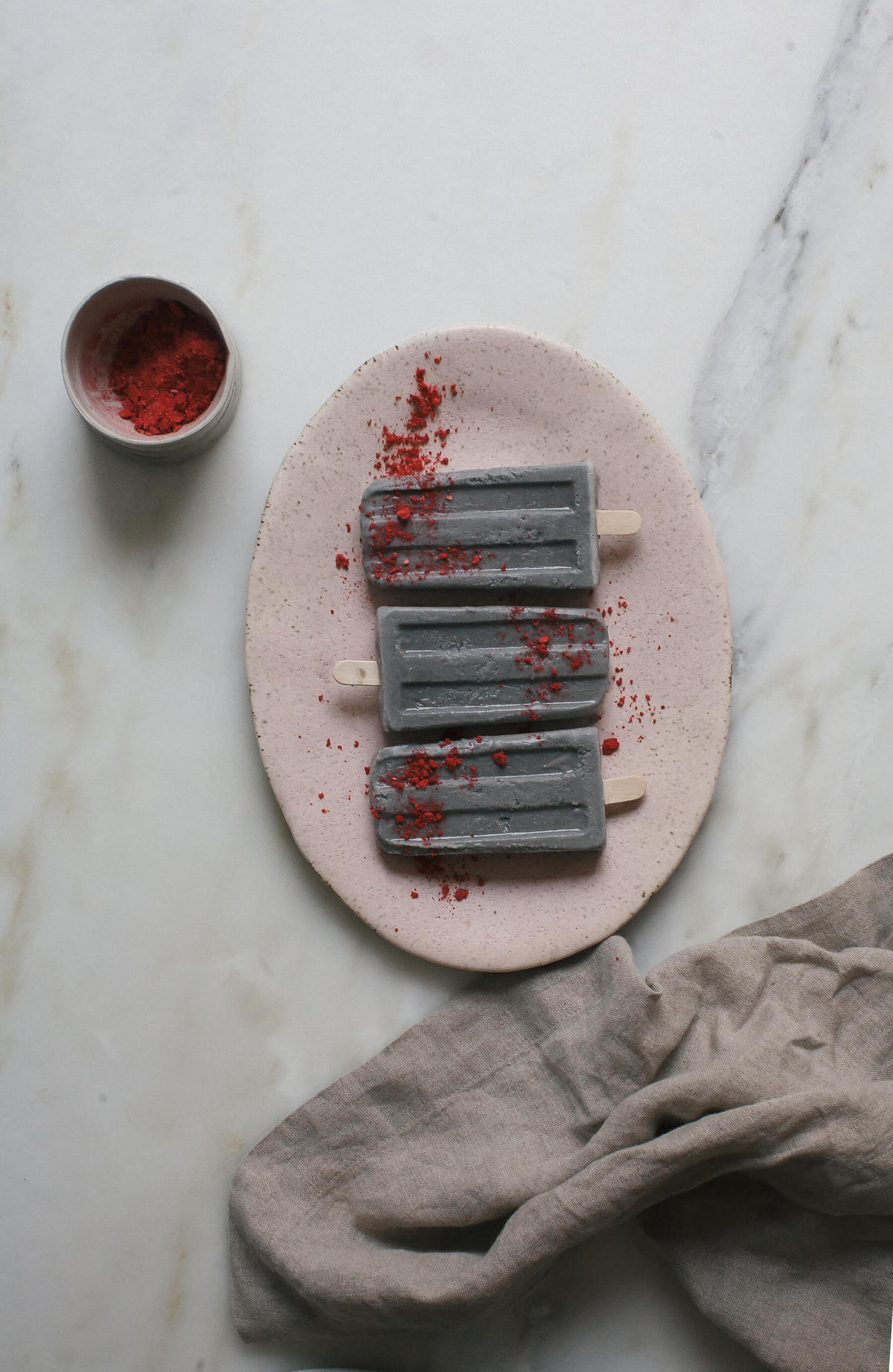 Black Sesame Popsicles on a platter topped with freeze dried strawberries.