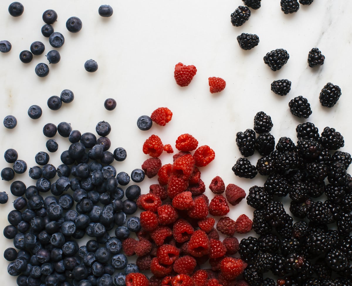 Fresh blueberries, raspberries and blackberries spread out on a counter. 