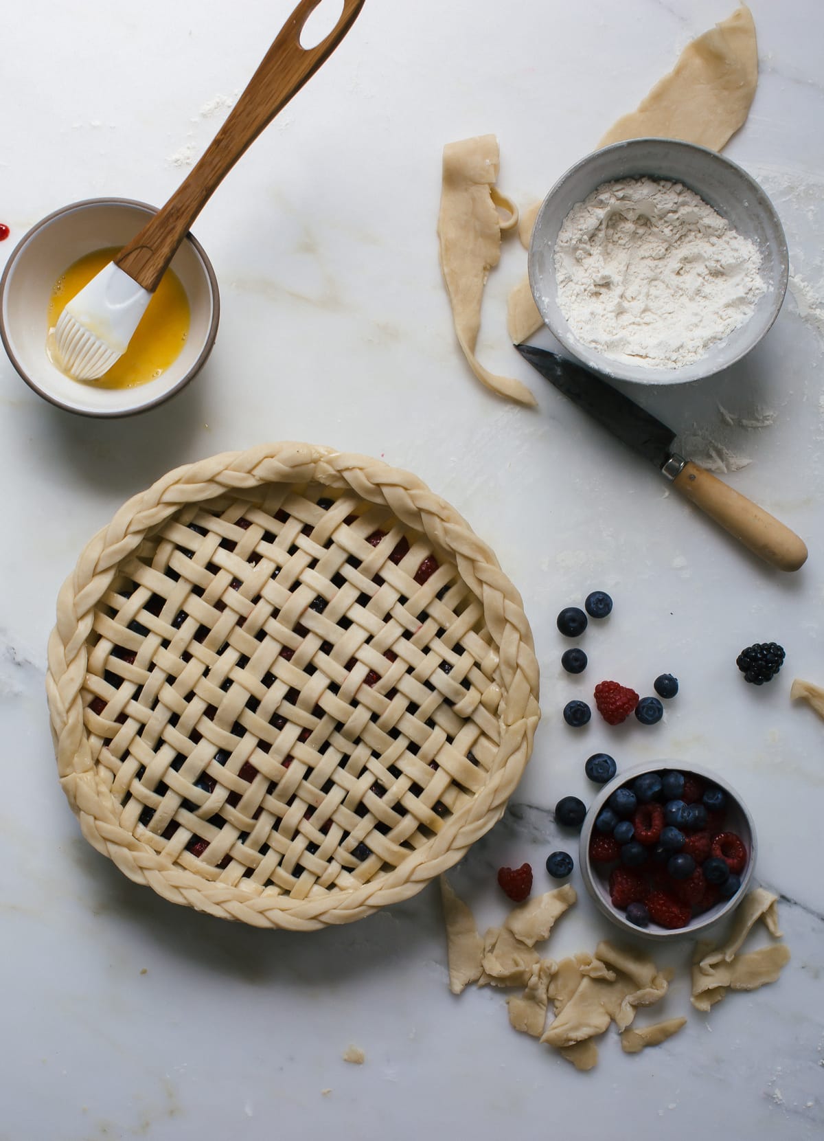 Unbaked lattice berry pie on a counter with a bowl of fresh berries near by. 