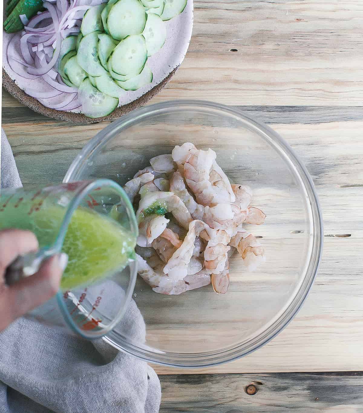 Chile water being poured over raw shrimp in a bowl.