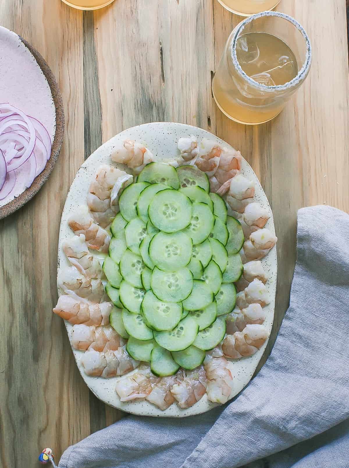 Shrimp on a platter with sliced cucumbers in the middle. 