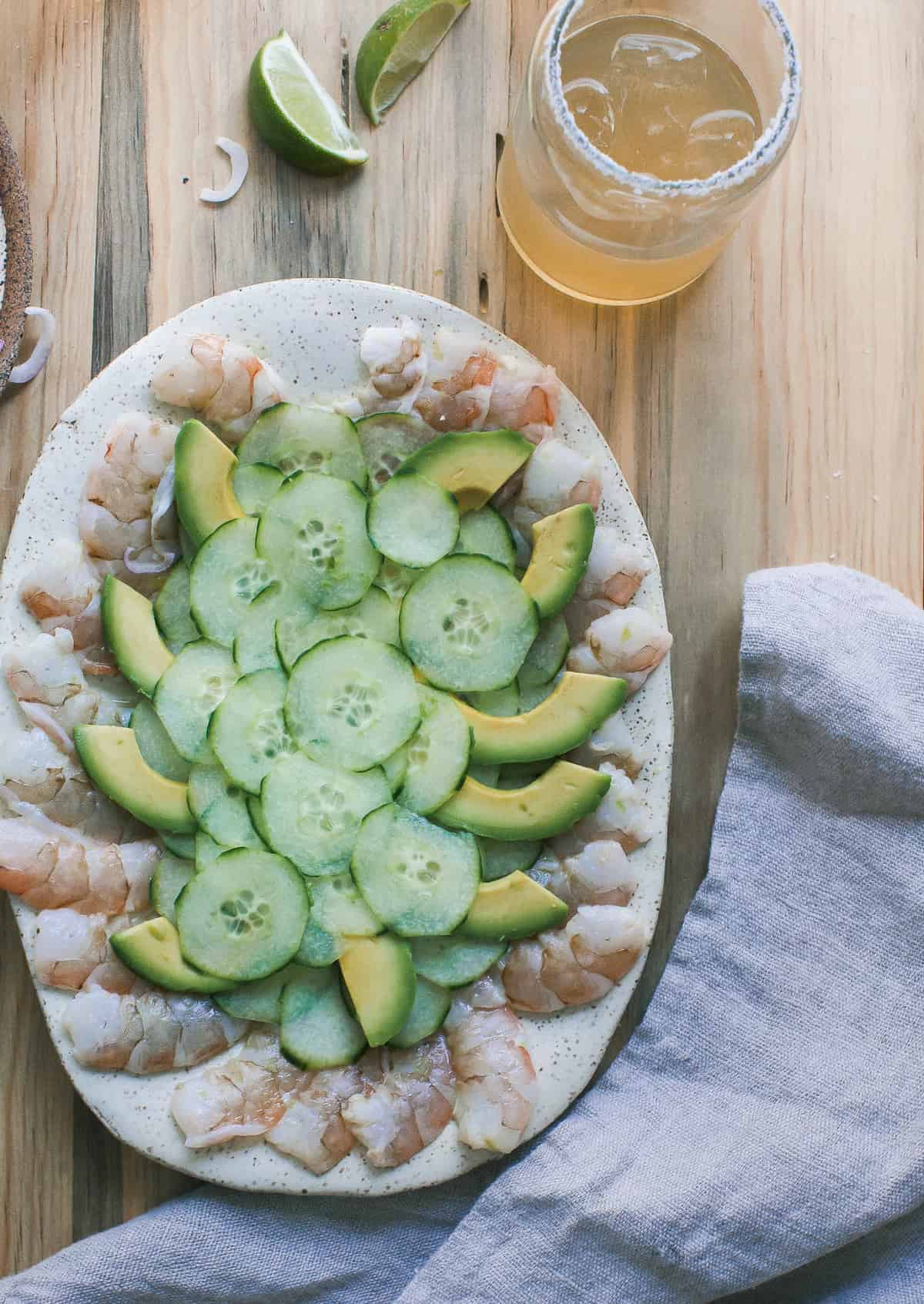 Aguachile on a platter topped with sliced cucumber and avocados.