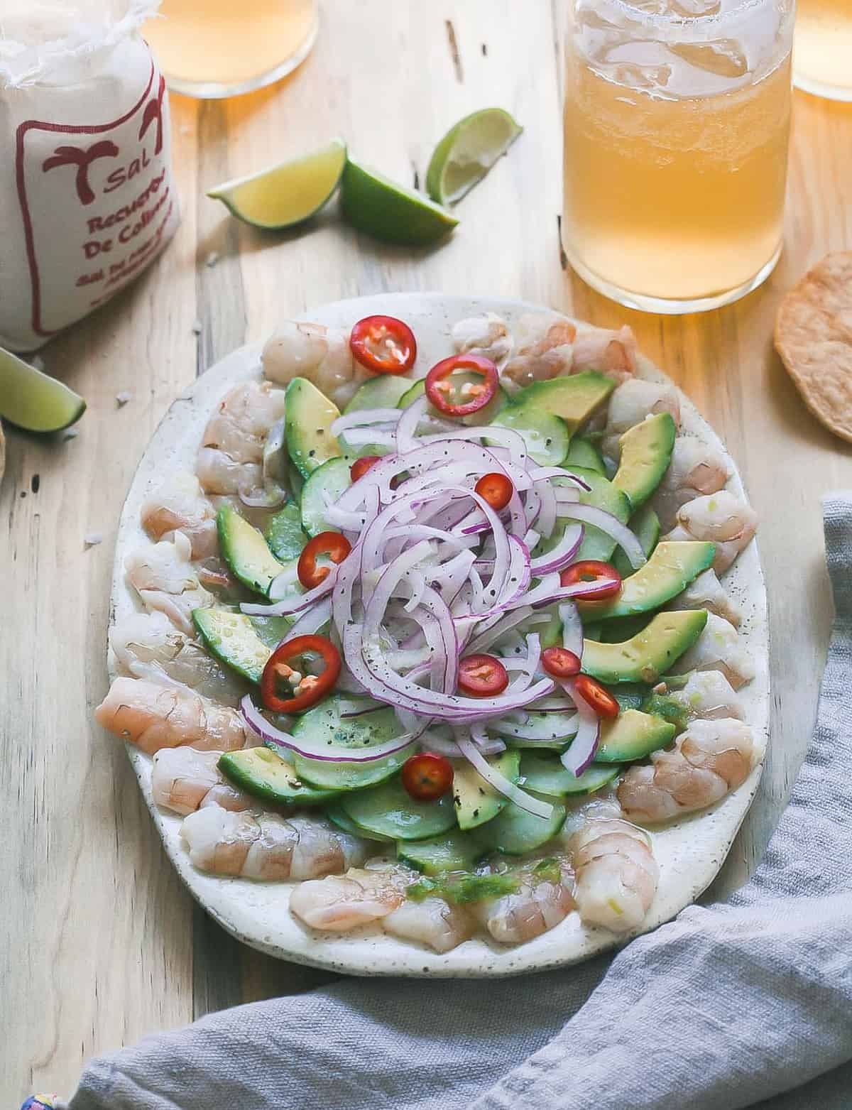 Raw shrimp appetizer on a plate with tostadas and beer near by.