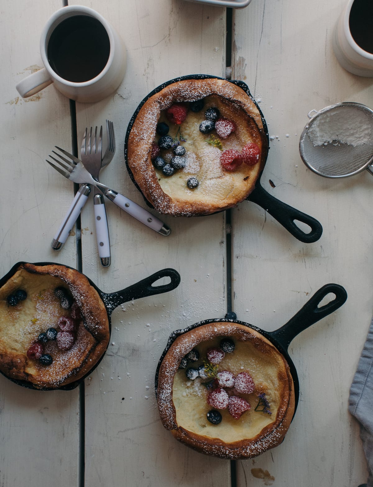 Baby Dutch Babies in skillets topped with fresh fruit and powdered sugar.