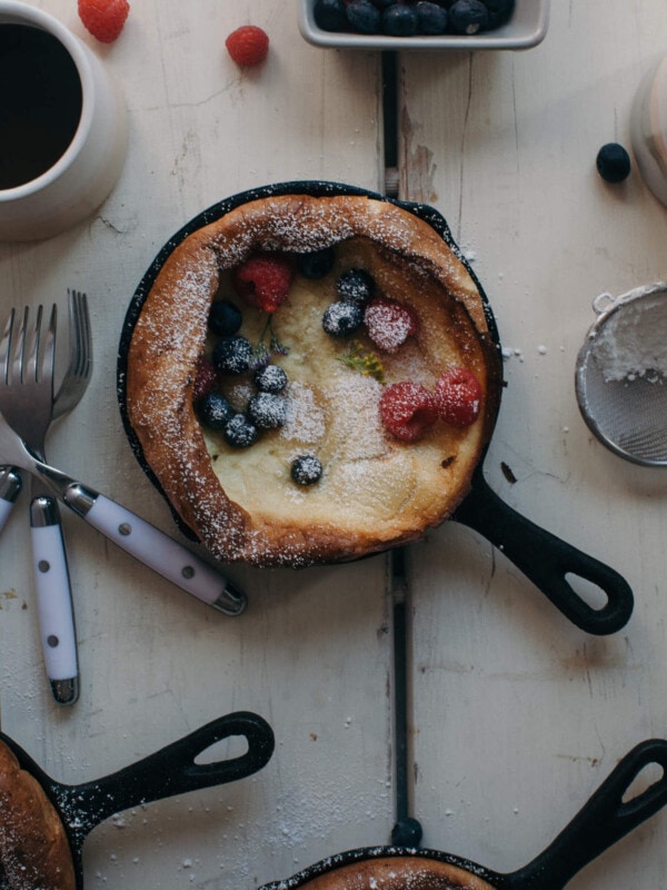 Close up image of a dutch baby in a skillet topped with powdered sugar and fresh berries.