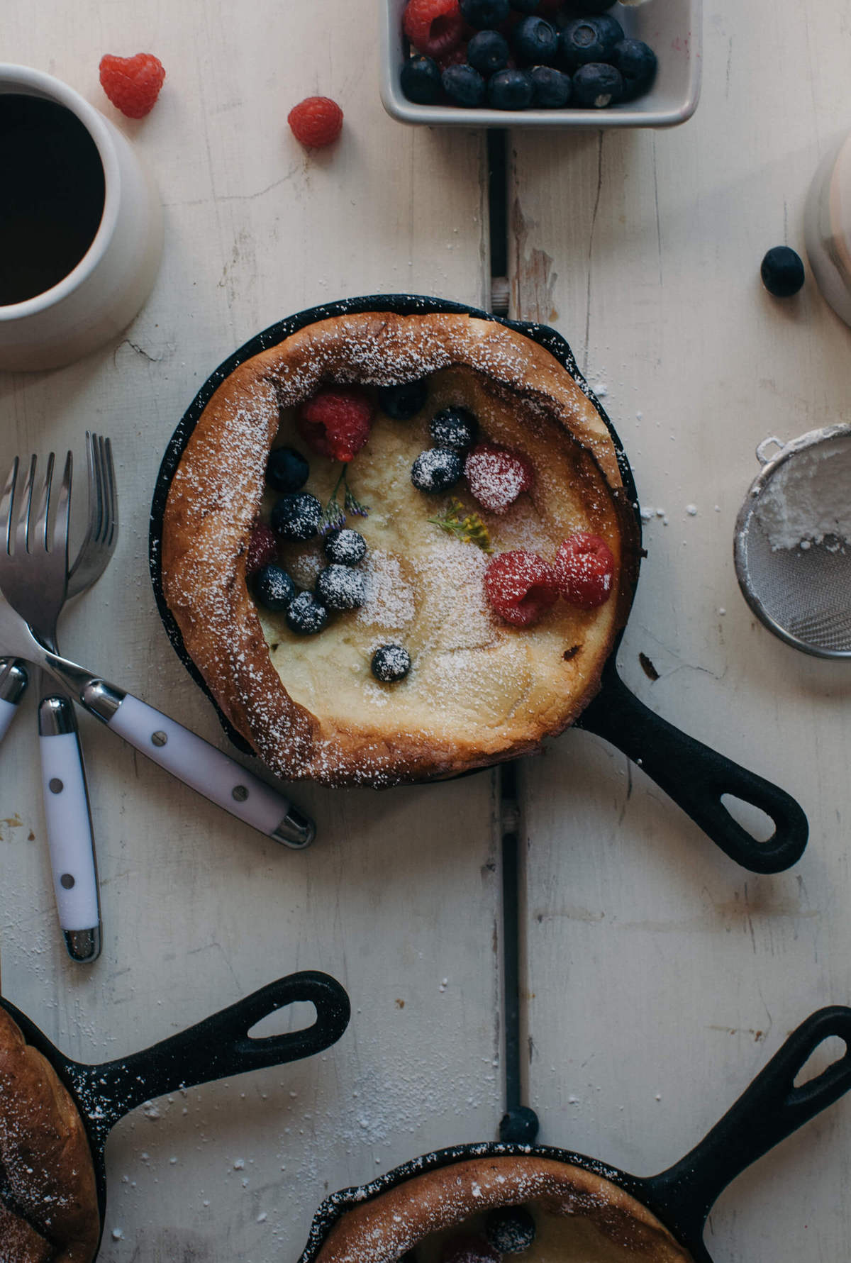 Close up image of a dutch baby in a skillet topped with powdered sugar and fresh berries. 