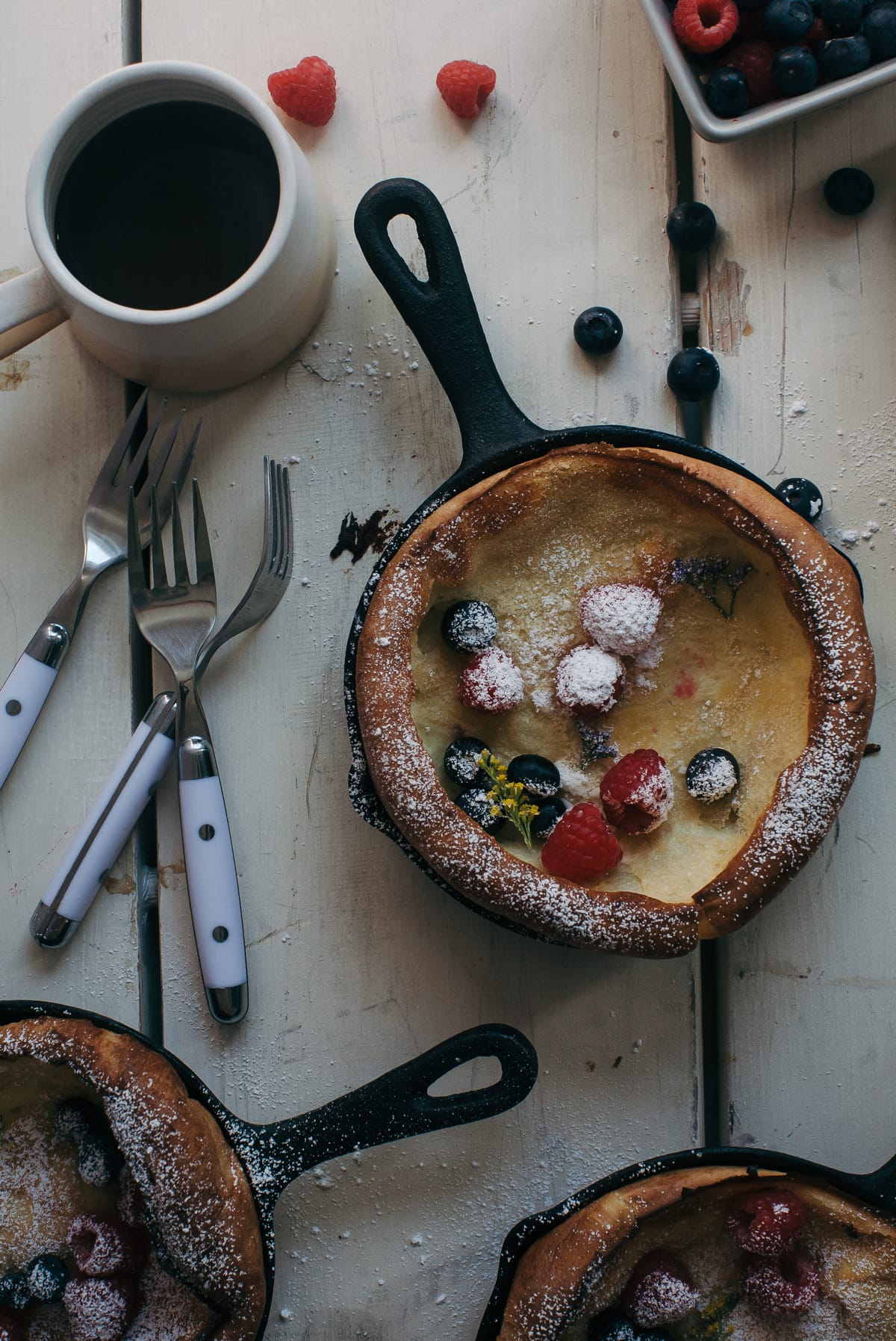 Eggy pancakes in skillets with utensils and coffee near by.