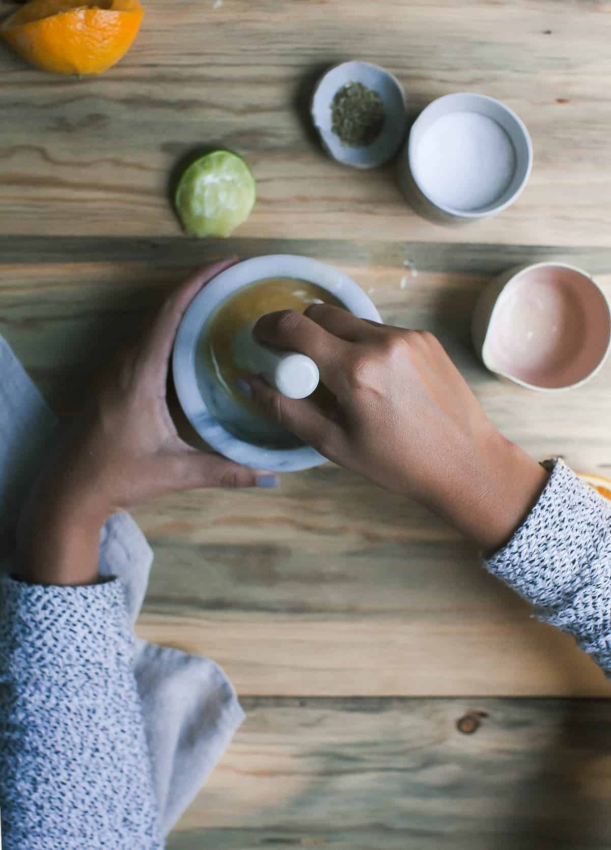 Hands mixing ingredients using mortar and pestle. 