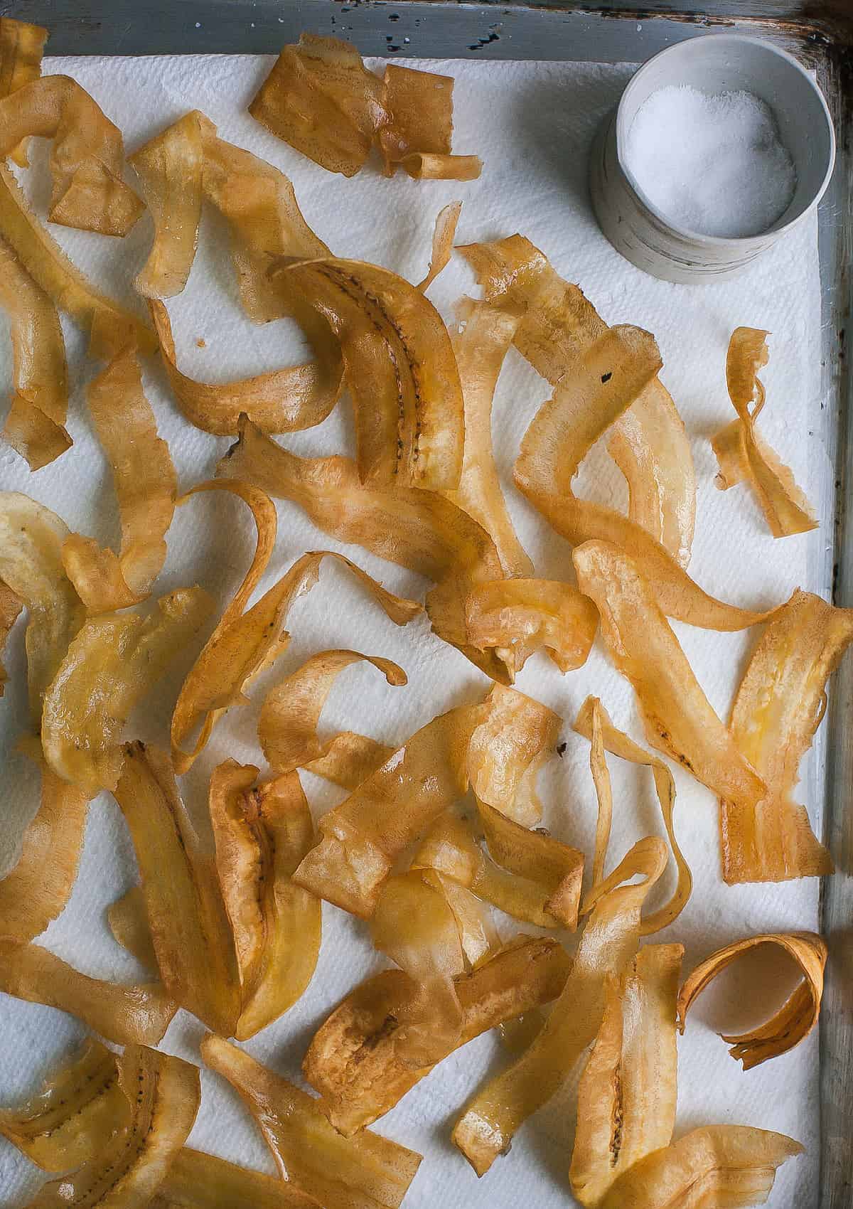 Close up image of crispy fried plantain chips on a sheet pan.