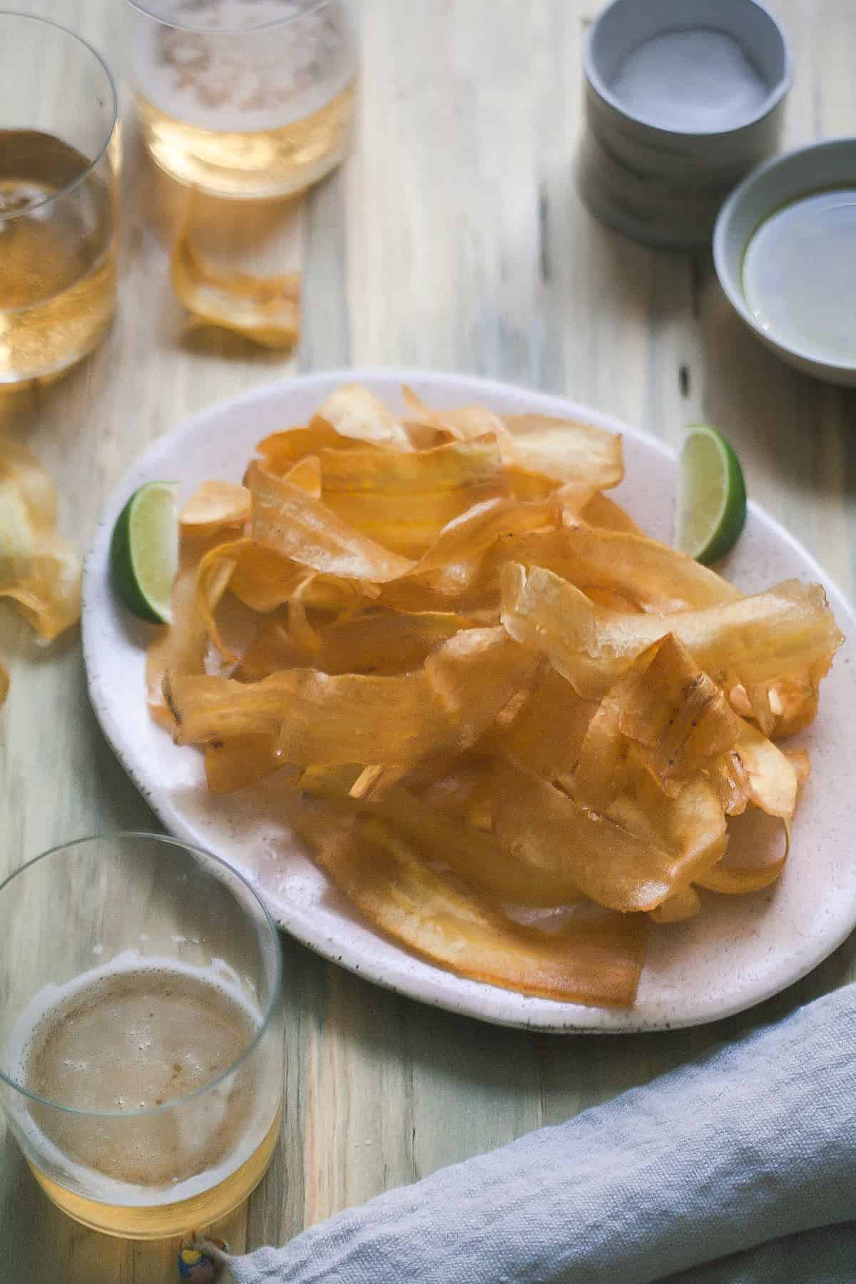 3/4 view of plantain chips on a plate with glasses of beer near by.