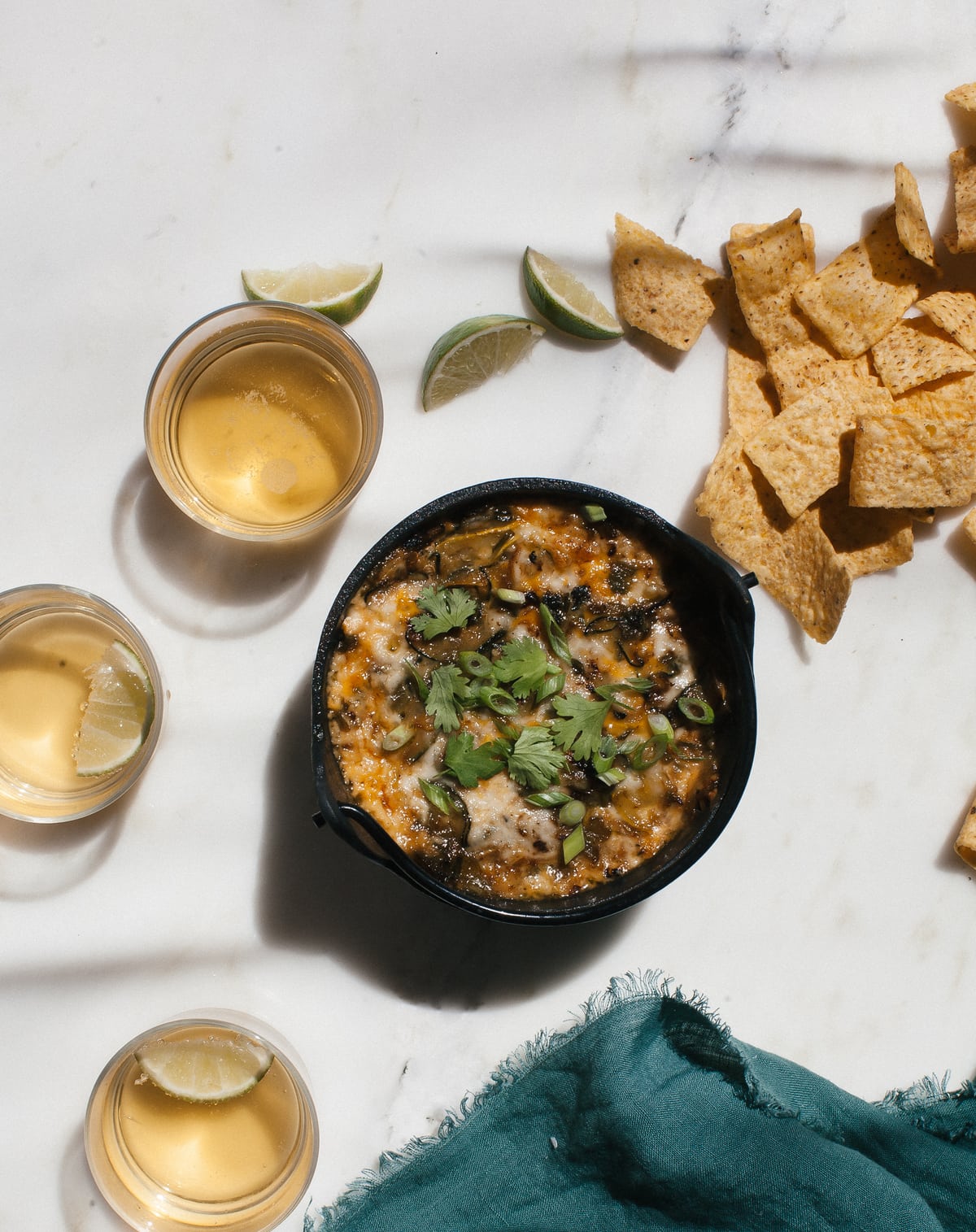 Summer squash queso fundido garnished with cilantro. Tortilla chips and beer near by.