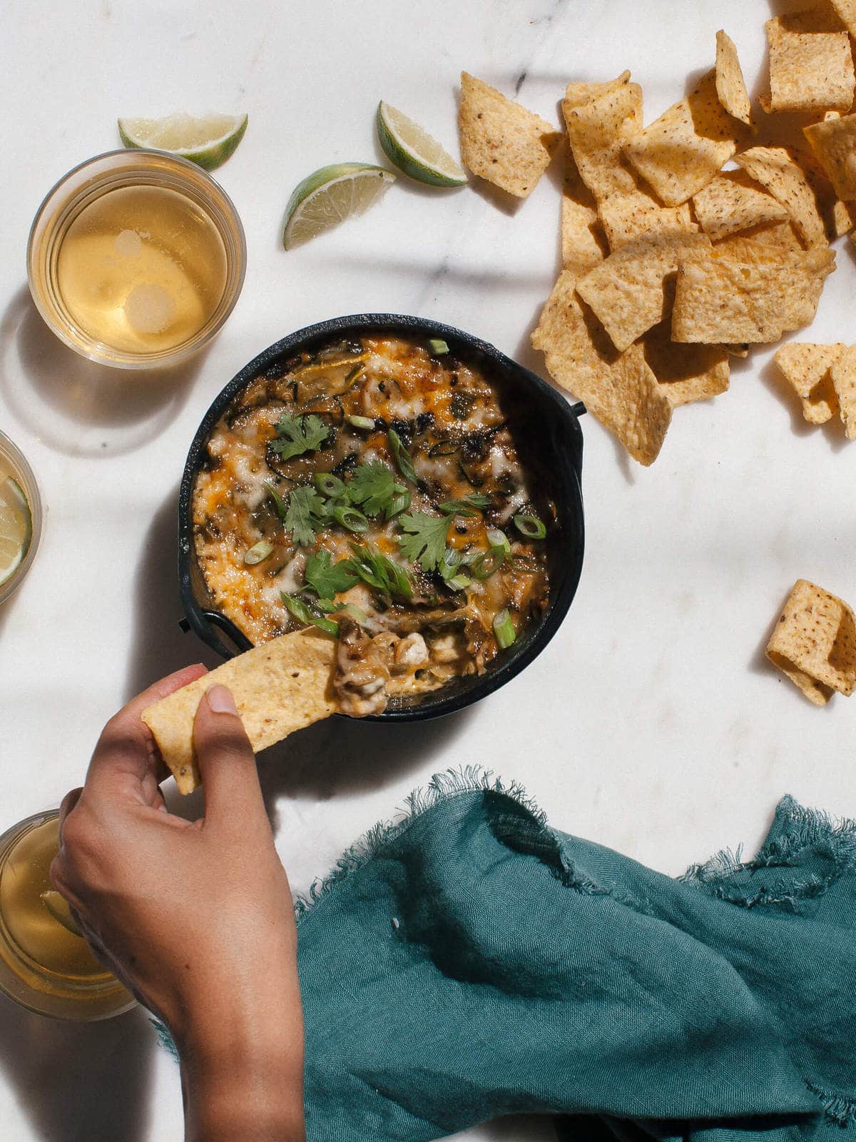 Hand scooping summer squash fundido with a tortilla chip.