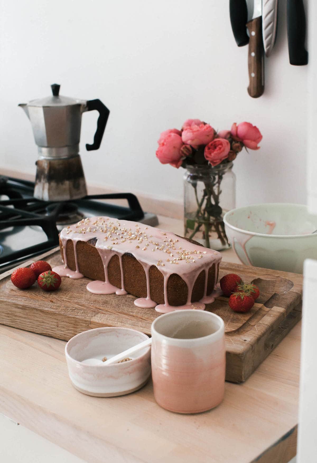 Close up image of a glazed strawberry rye loaf on a cutting board with fresh strawberries.