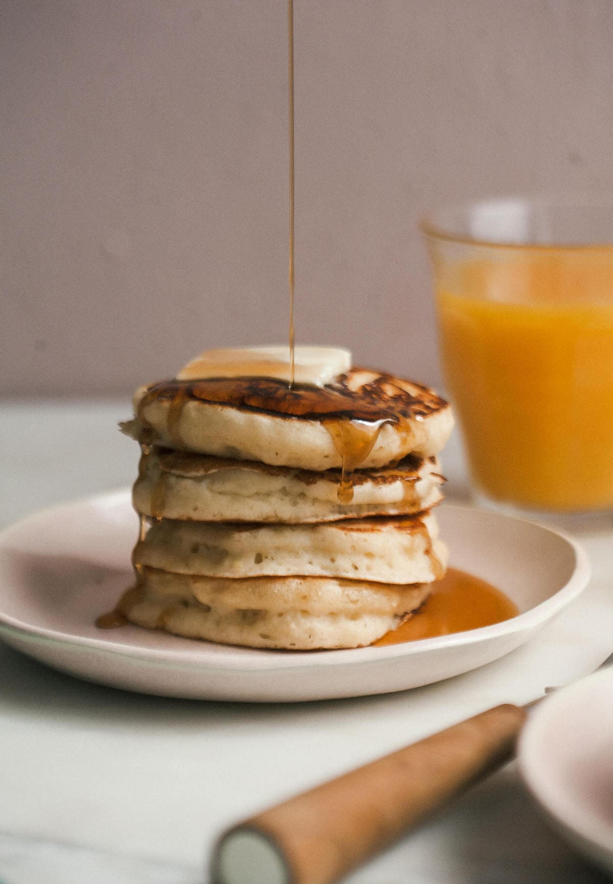 Stack of lemon ricotta pancakes on a plate being drizzled with maple syrup.