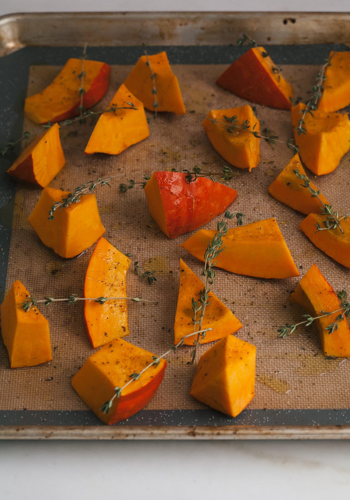 Sliced squash on a baking sheet topped with fresh sprigs of thyme.