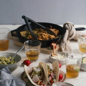 Side view of chicken fajitas on a plate with glasses of beer near by.