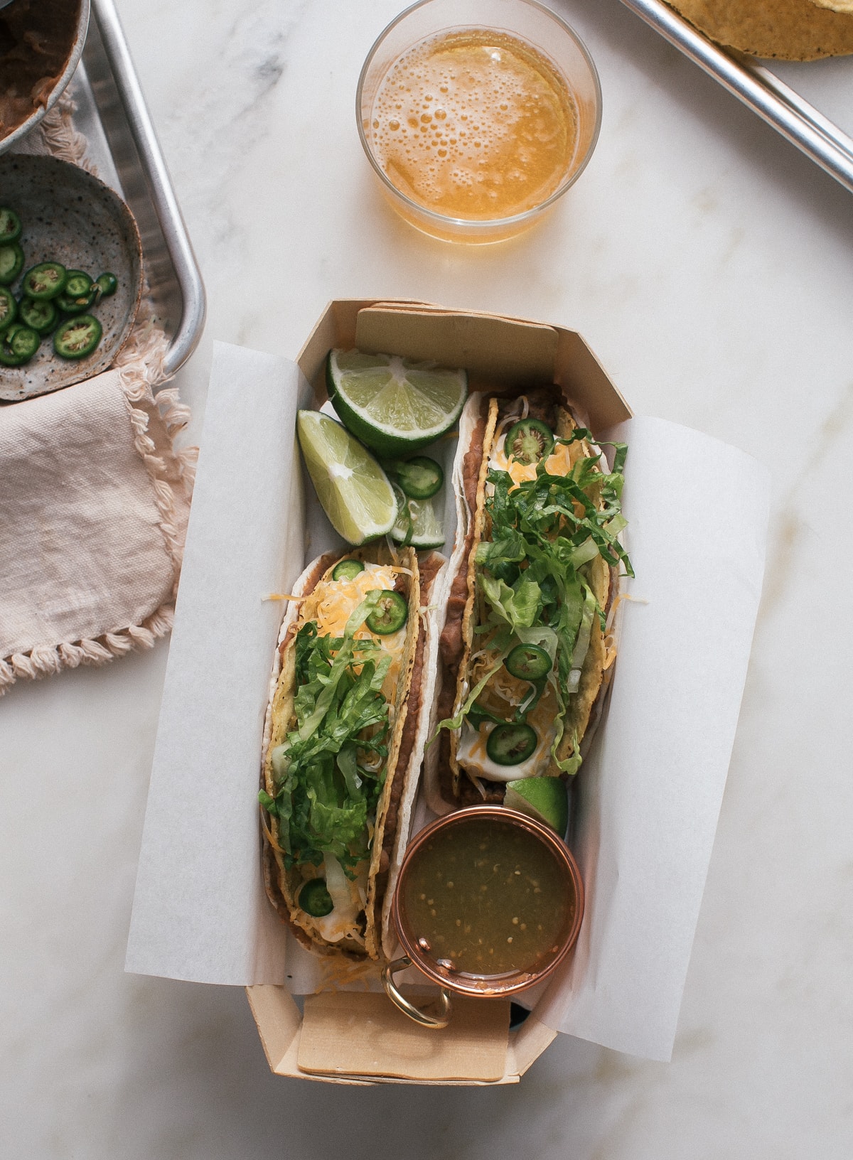 Overhead image of double decker tacos in a box with a drink nearby.