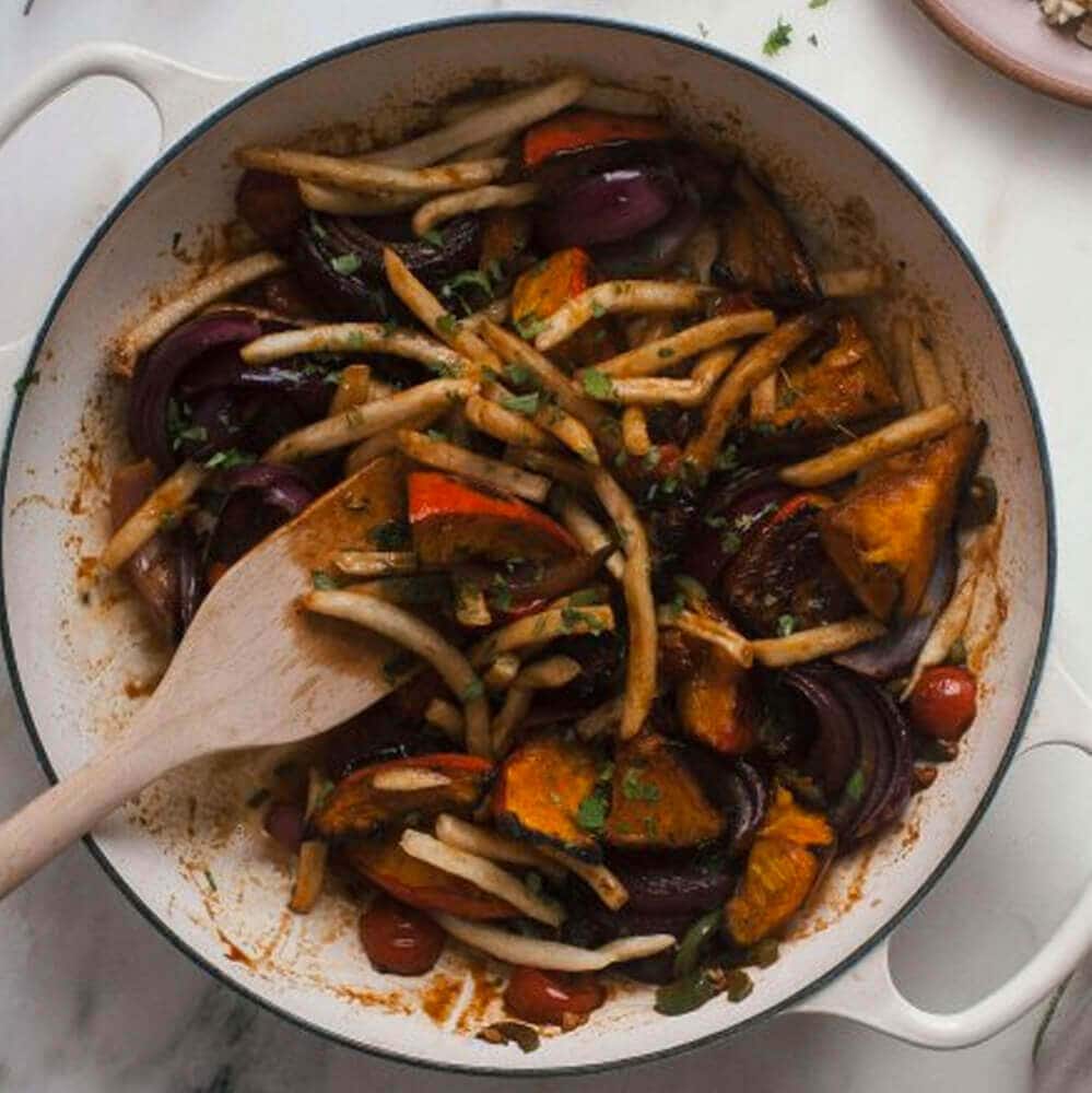 Close up image of squash and fries in a skillet with a wooden spoon.