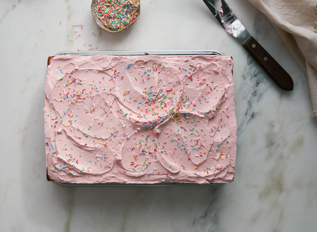 Strawberry sheet cake with rhubarb frosting on a counter with a spatula near by.