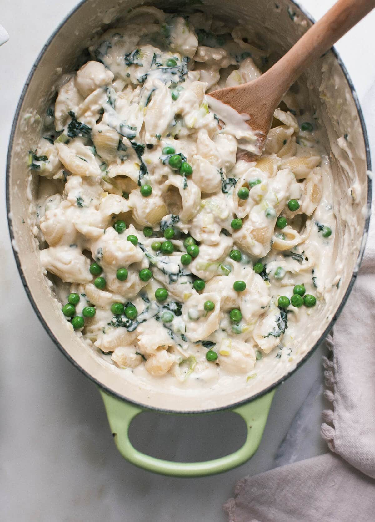 Stovetop macaroni and cheese topped with peas in a pot with a wooden spoon.