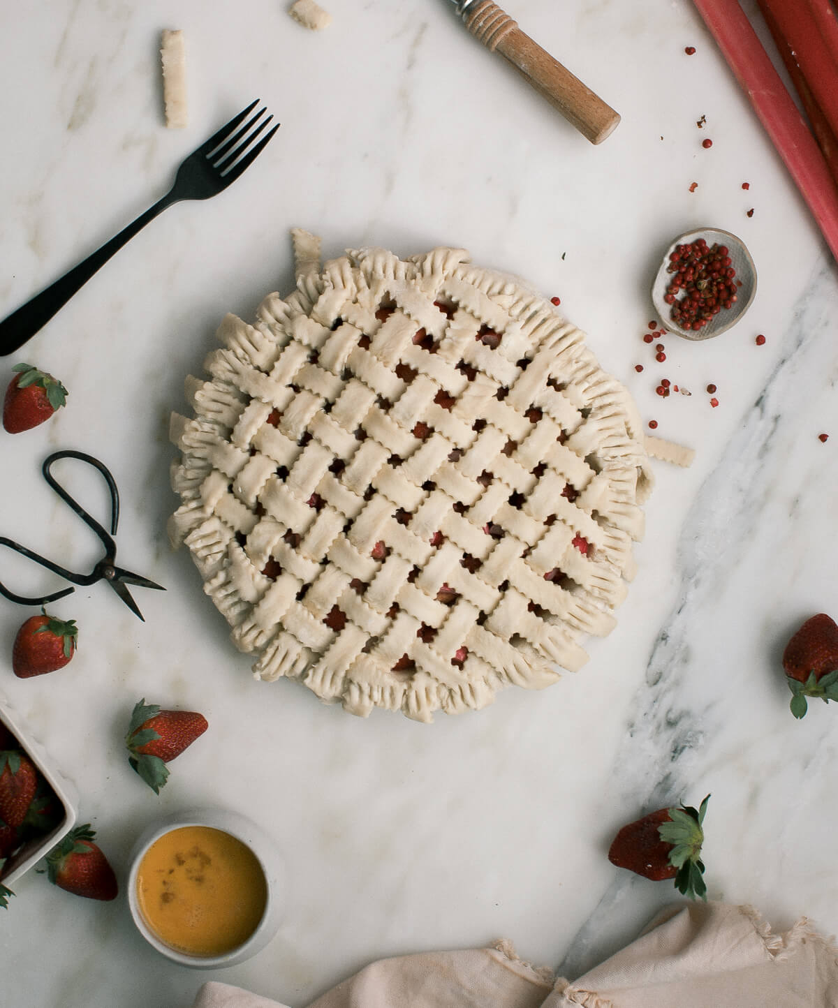 Unbaked pie with a lattice pie crust and pie ingredients all around.